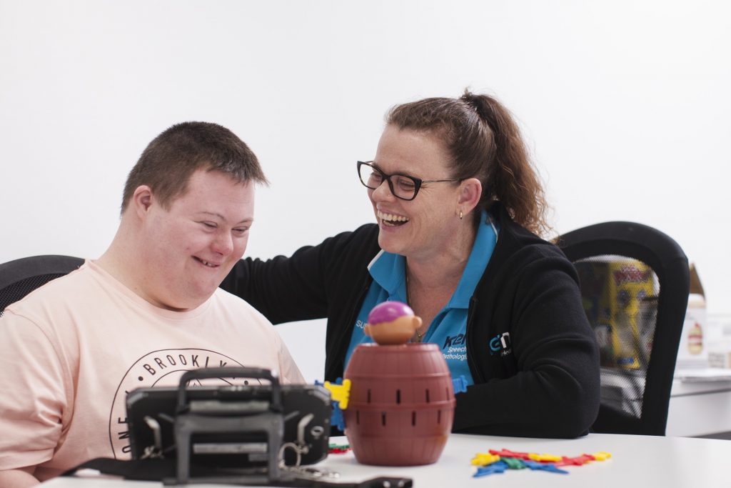 An NDIS speech pathologist congratulates a client on his progress with a smile and pat on the back