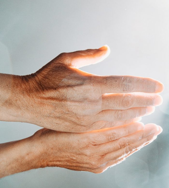 An elderly person cups their hands in the sunlight