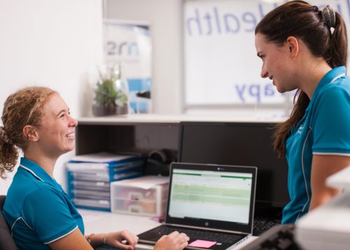 Two allied health staff talk to each other at their work desk
