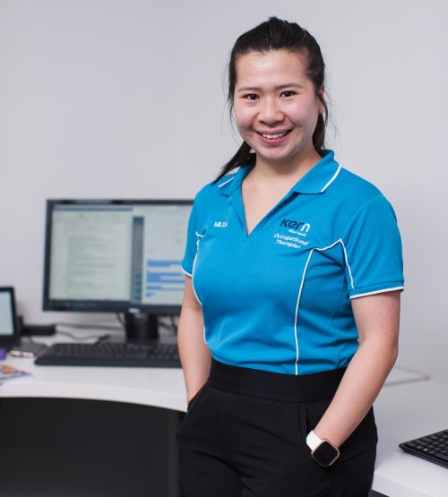 A Kern Allied Health occupational therapist smiles while leaning against her work desk